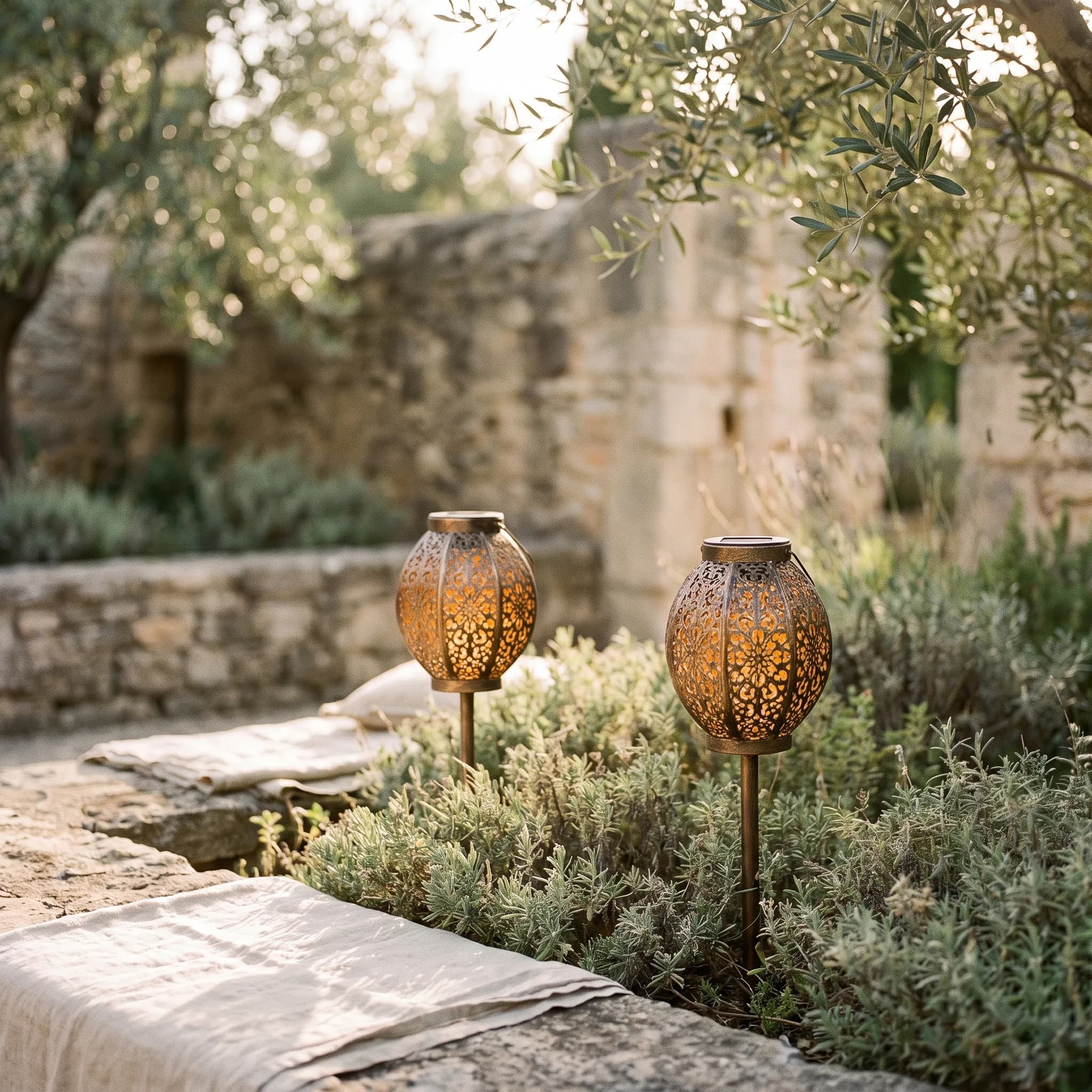 Two ornate cut-metal solar stake lights glowing warm amber at dusk among low green foliage